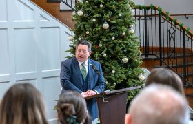 person at a podium in front of a Christmas tree