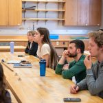 students sitting at table listening to professor speak
