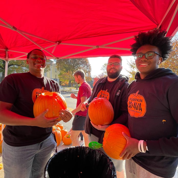 three students scooping out pumpkin guts